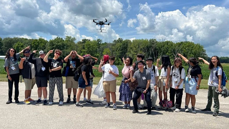 A group of Summer Residential campers point to a drone flying overhead
