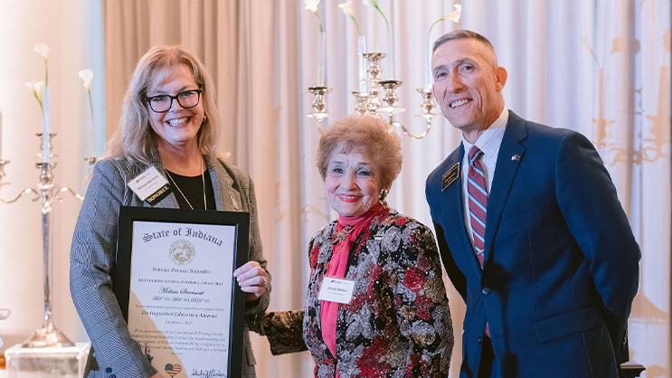 Phillip VanFossen, Sheila Klinker, and alumna Melissa Stormont smiling for a photo. Stormont is holding a large award certificate.