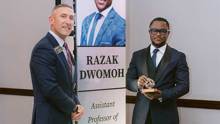 Phillip VanFossen and Razak Dwomoh standing in front of a banner with Dwomoh's name and photo.
