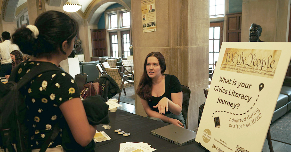 A Constitution Day attendee speaking to a representative. On a table between them is a poster titled, 