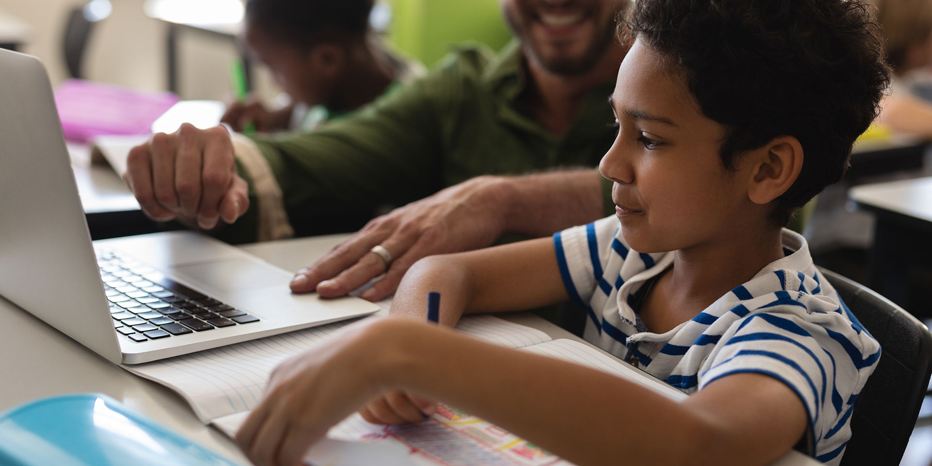 A teacher works with a young male student on a laptop