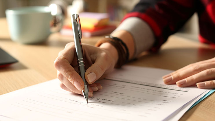 A hand with a pen is shown writing something on a piece of paper
