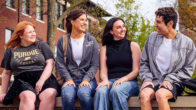 A group of Purdue University students talk outside a campus building
