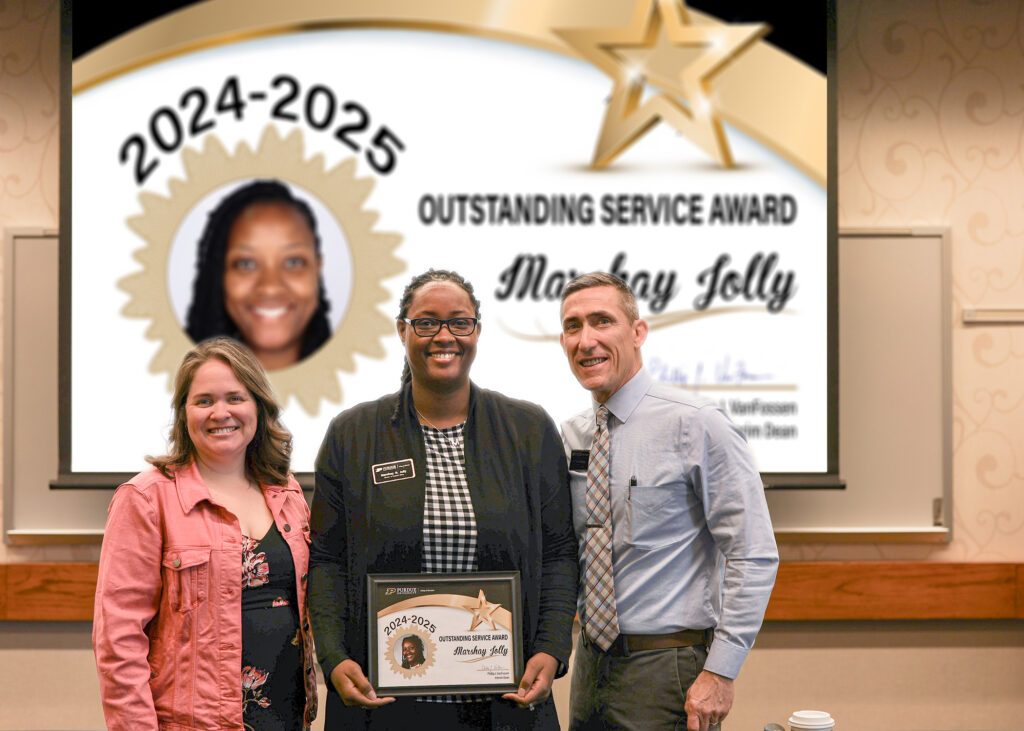 Marshay Jolly holding a certificate. Standing with her are Jennifer Smith and Phillip VanFossen.