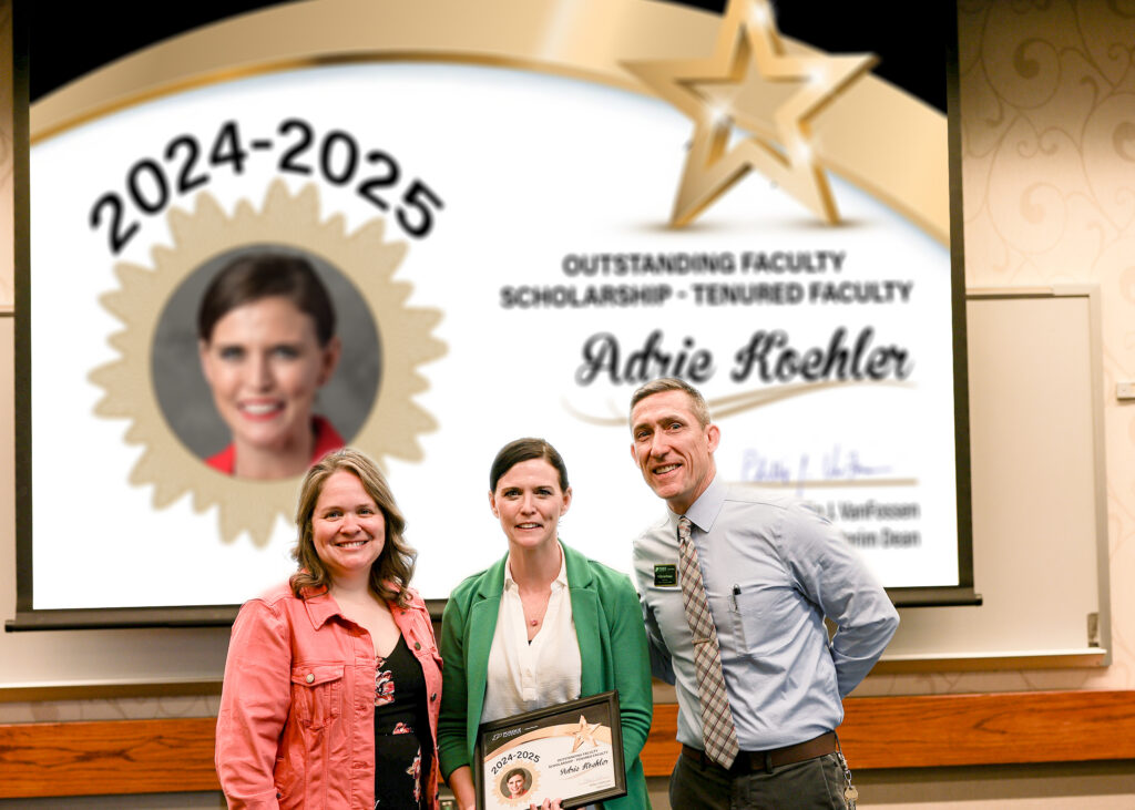 Dr. Adrie Koehler holding a certificate. Standing with her are Jennifer Smith and Phillip VanFossen.