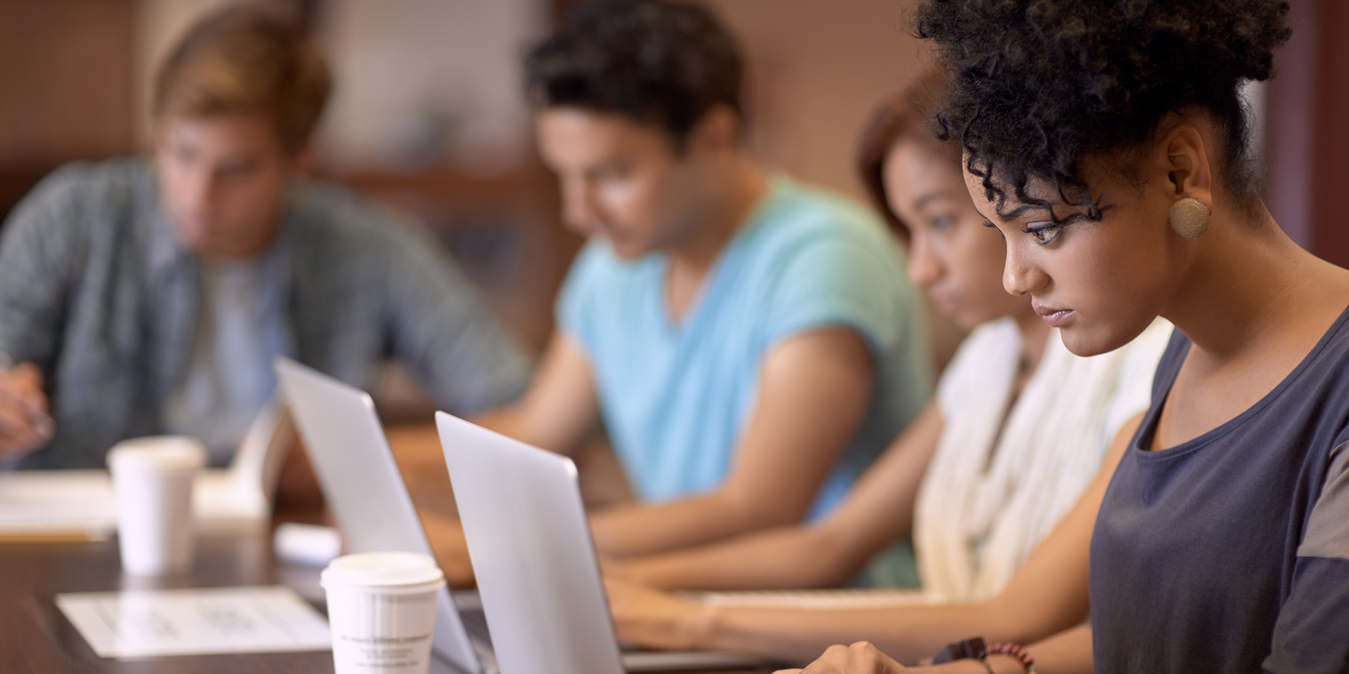 A group of young adults seated in a library using their laptops.