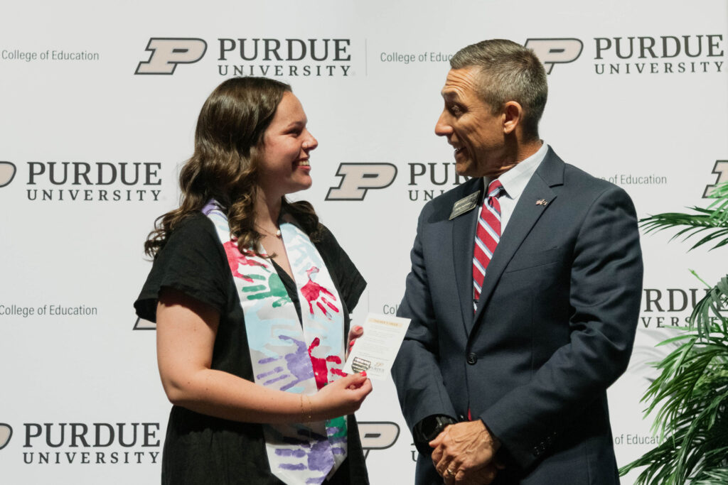 Haven Baker and Phil VanFossen looking at each other and smiling. Haven is wearing a black dress with a colorful handprint stole and Phil is wearing a navy suit with a red striped tie. 