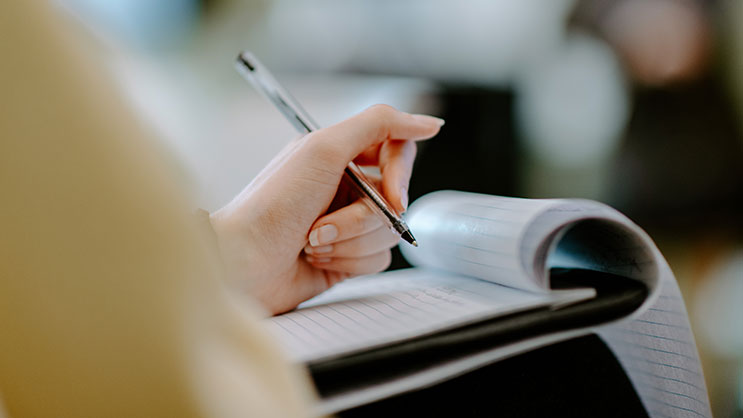 A hand holds a pen and writes notes on legal pad