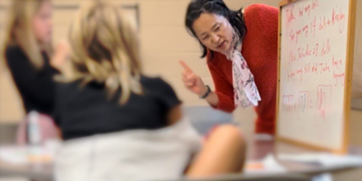 Yan Ping Xin writing on a whiteboard in front of two elementary students.