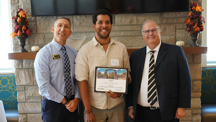 Carlos Trotman holding a certificate. He is surrounded by Phil VanFossen and Wayne Wright.