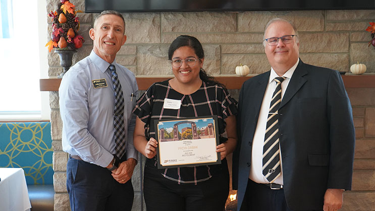 Priya Dabak holding a certificate. She is surrounded by Phil VanFossen and Wayne Wright.