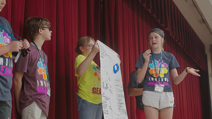 Four students standing on a stage and presenting a poster.
