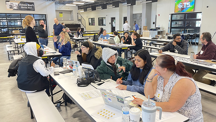 A group of workshop attendees seated in a cafeteria in a high school. 