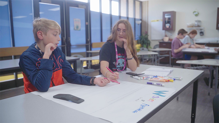 Two GEAR UP students seated at a desk, creating a poster.