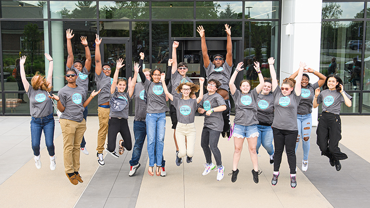 A group of GEAR UP students jumping outside in front of a building.