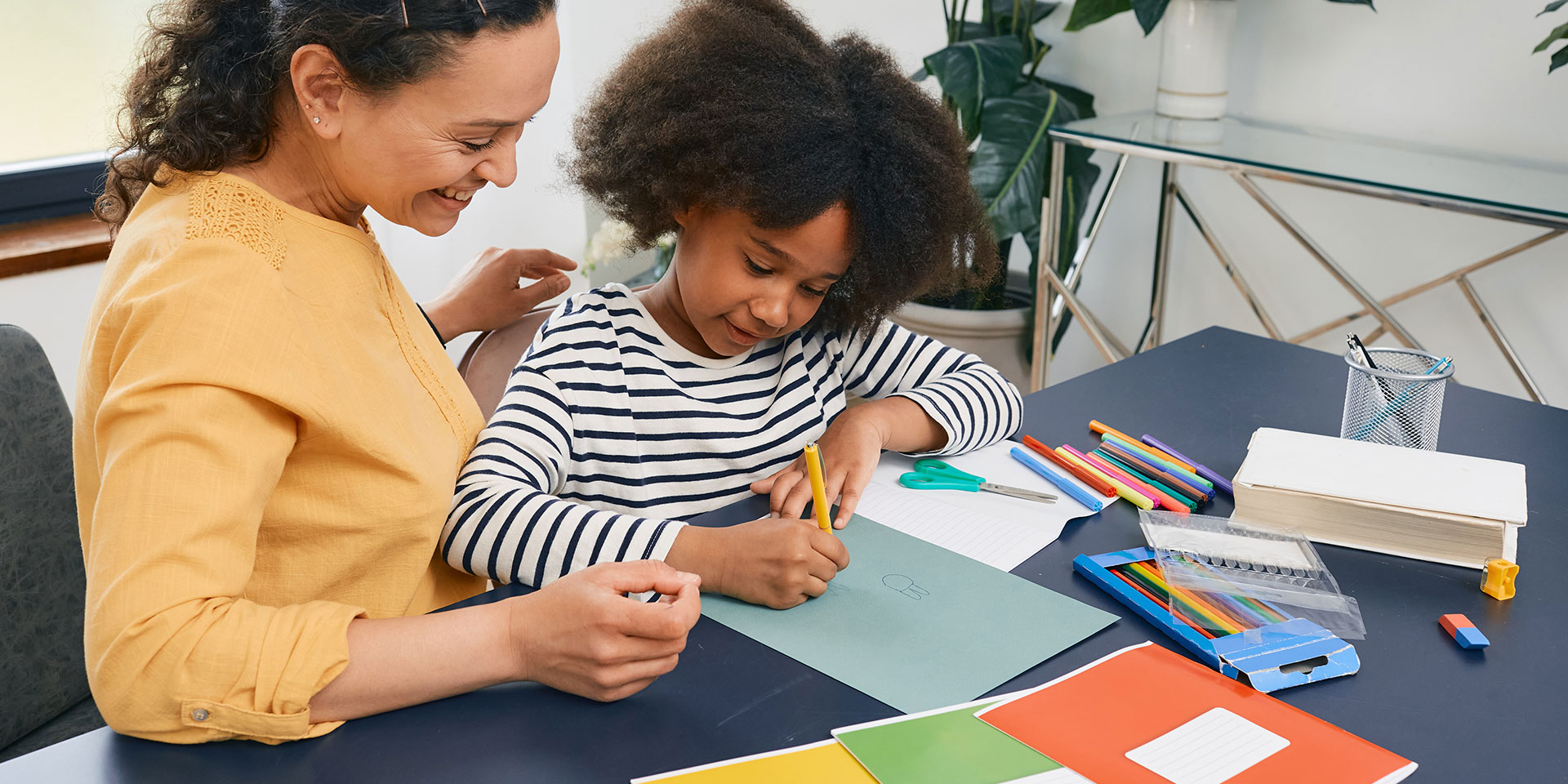 A female teacher works with a young female student on a classroom project.