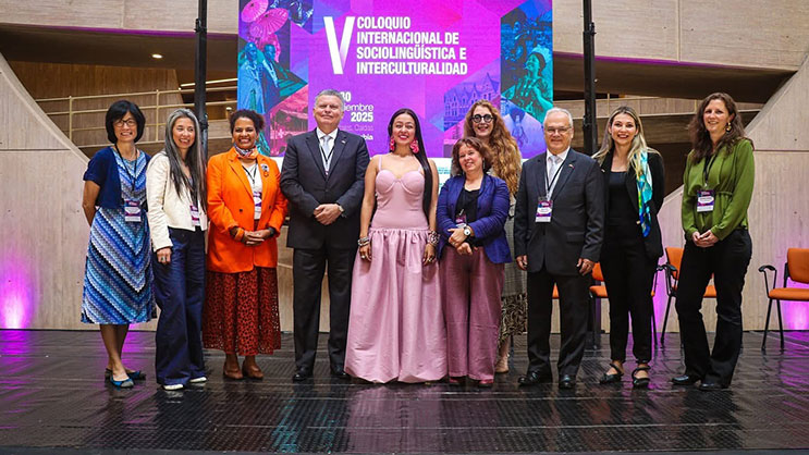 A group of nine people standing on a stage. Behind them is a presentation titled 