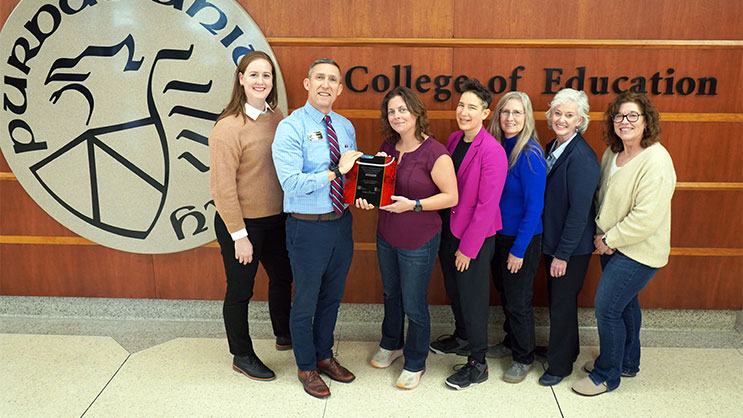 Phil VanFossen and six ELRC staff members standing in the main lobby of Beering Hall. They are holding a plaque inscribed with the Kellogg Award.