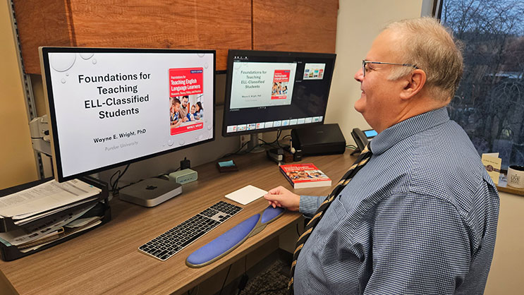 Wayne Wright seated at a desk in an office. He is looking at a PowerPoint presentation on his computer screen.