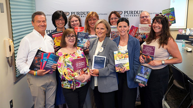 A group of 10 faculty holding their books in front of a College of Education backdrop.