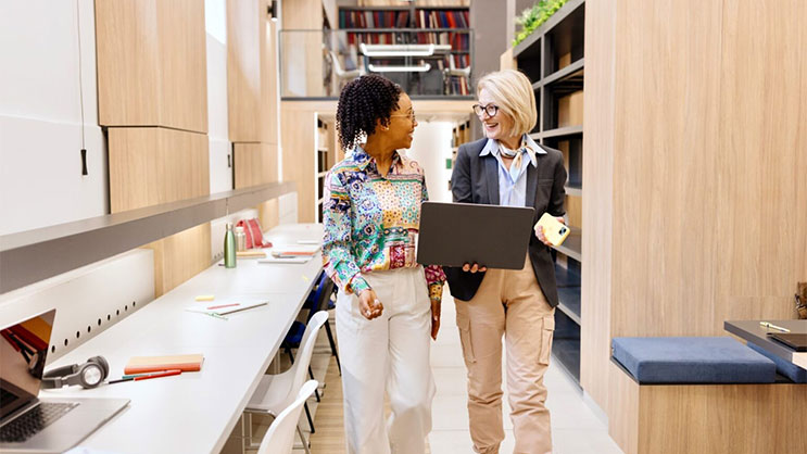 Two teachers facing each other and smiling in a classroom.