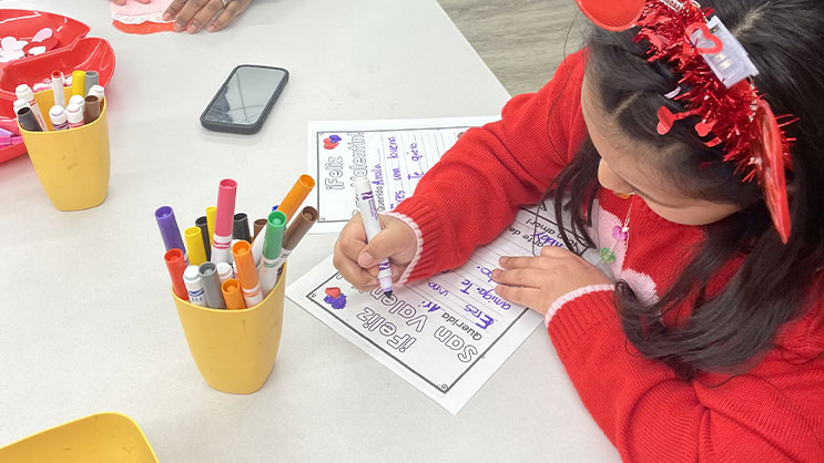 A child holding a purple marker while writing on a coloring page.