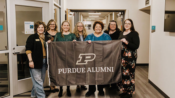 Five 2026 Golden Apple Award winners with Tara Star Johnson and Erin Perdue. All are holding a banner that says "Purdue Alumni".