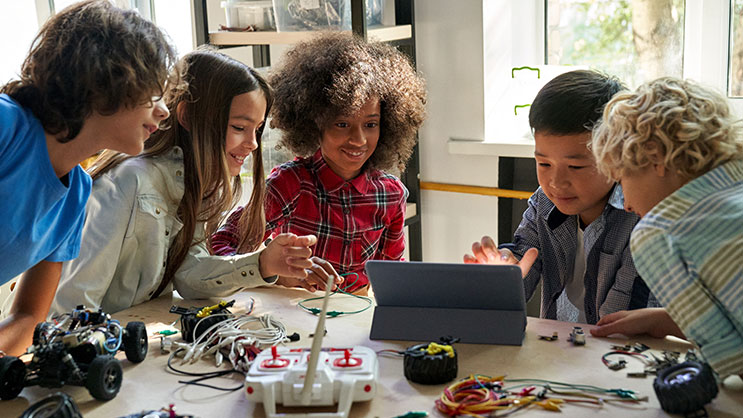 A group of middle school students work on a robotics project using a tablet.