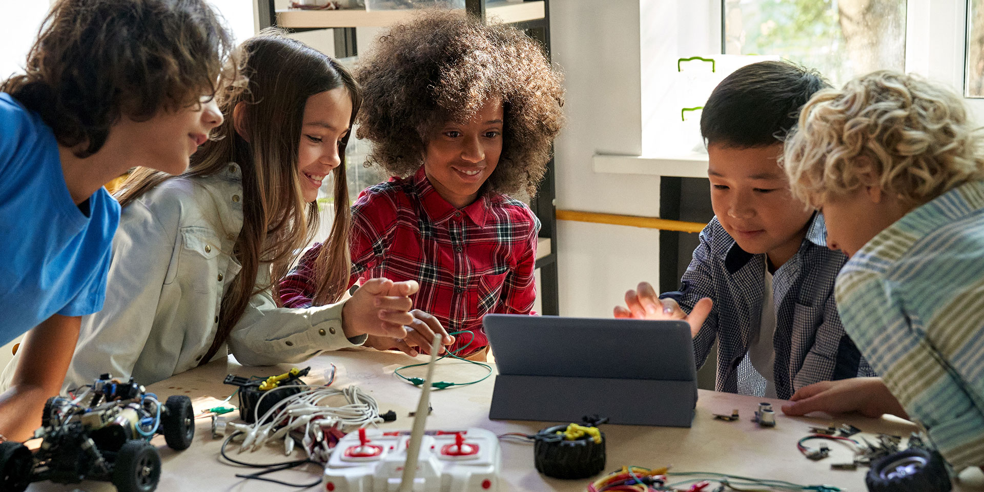 A group of middle school students work on a robotics project using a tablet.