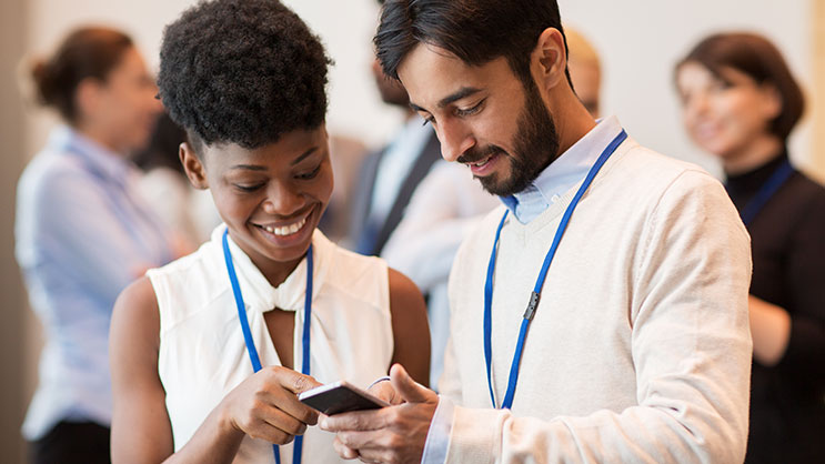 A man and woman look at a smartphone during a conference.
