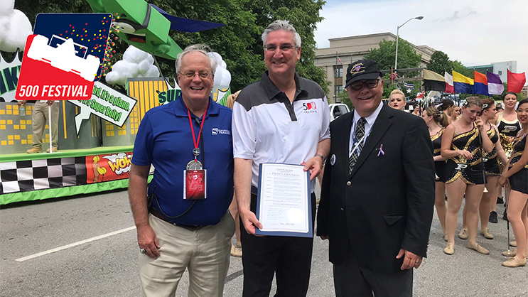 Mark Eutsler, Eric Holcomb, and Jay Gephart standing outside in front of a parade.