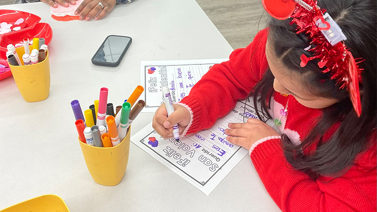 A young girl writes and colors in a worksheet with a marker.