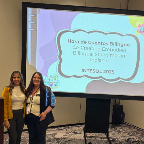 Brenda Sarmiento Quezada and Dafne Zanelli stand in front of a projector featuring a conference presentation.