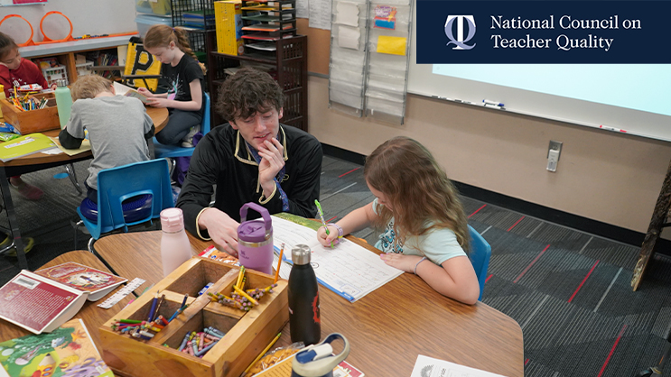 A Purdue student teacher sitting at a desk with an elementary school student.