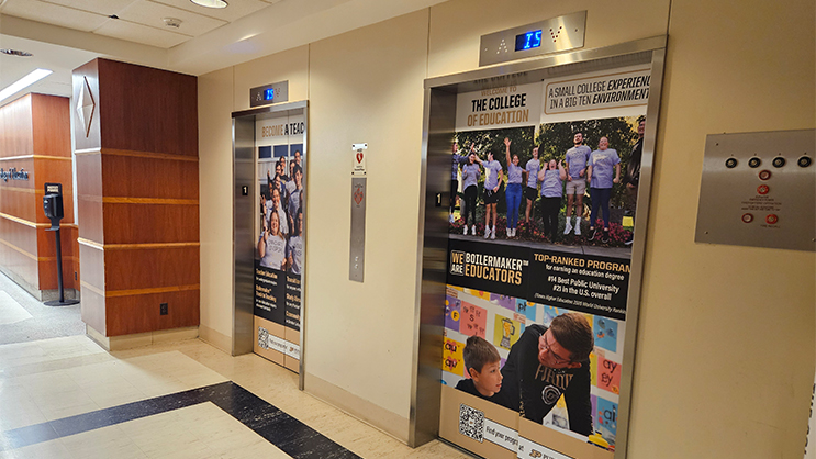 A pair of elevators in a building. The doors are wrapped in a College of Education graphic.