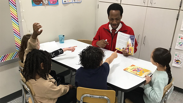 Gregory Butler reading a book to a group of four schoolchildren. 