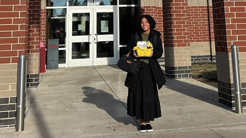 Jordan Garrison holding a yellow basket outside of a brick building. 