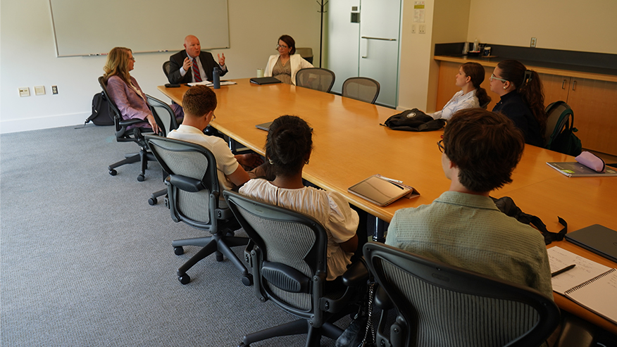 A group of five students seated at a long table in a conference room. At the head of the table are three Indiana judges. 