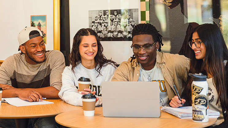 Four students work on a project using a laptop