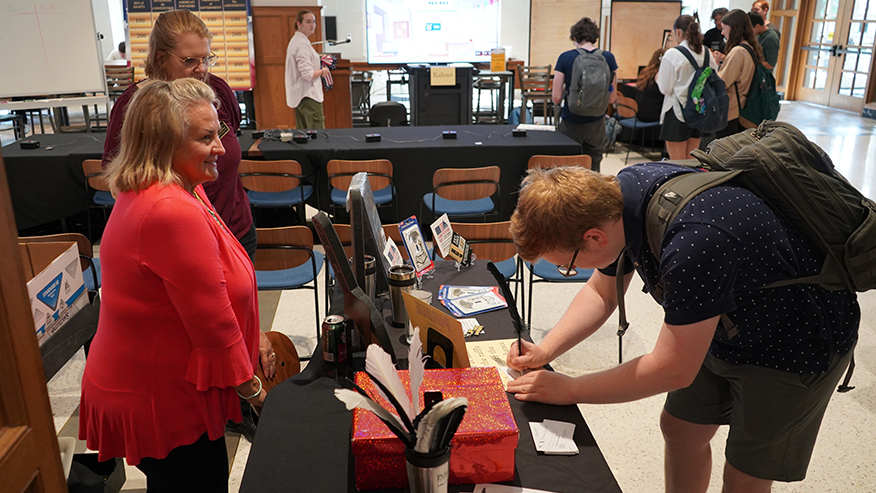 A student bent over a table signing a piece of paper with a quill. 