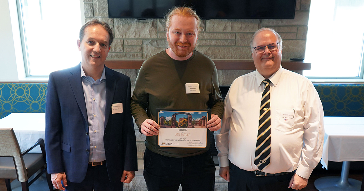 Jon Butler holding a certificate. He is surrounded by Nielsen Pereira and Wayne Wright.