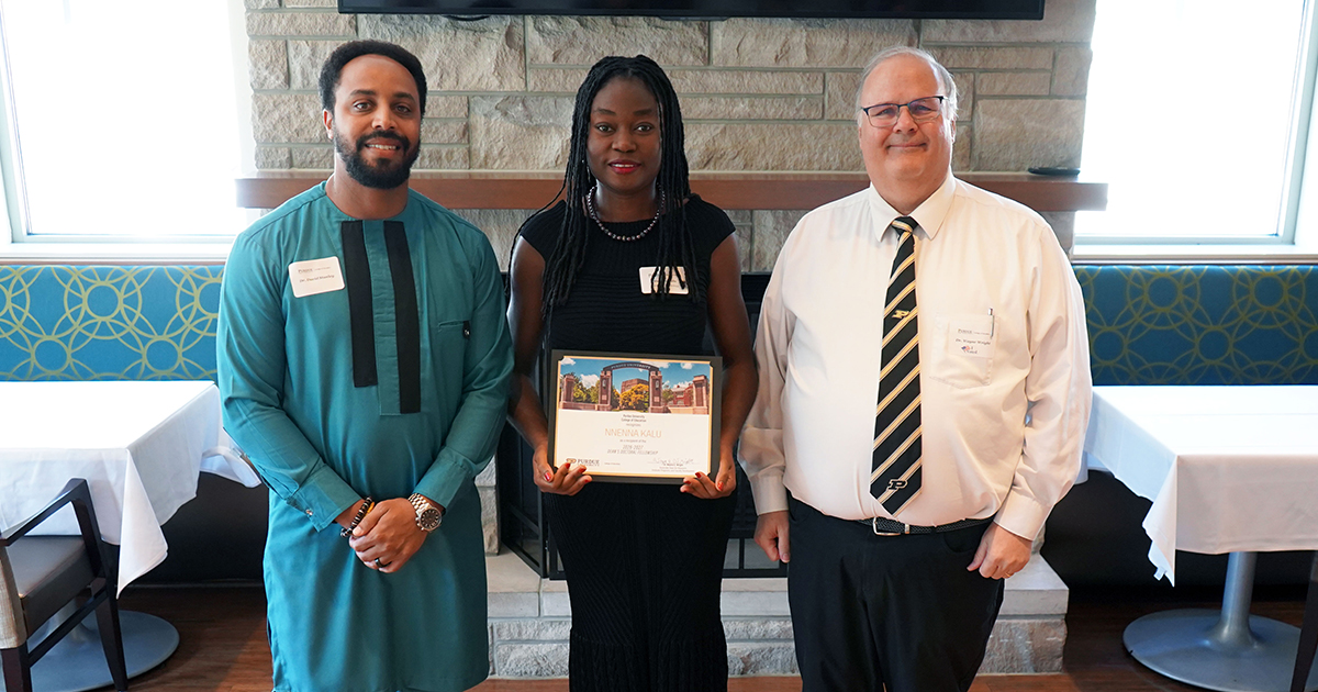 Nnenna Kalu holding a certificate. She is surrounded by David Stanley and Wayne Wright.